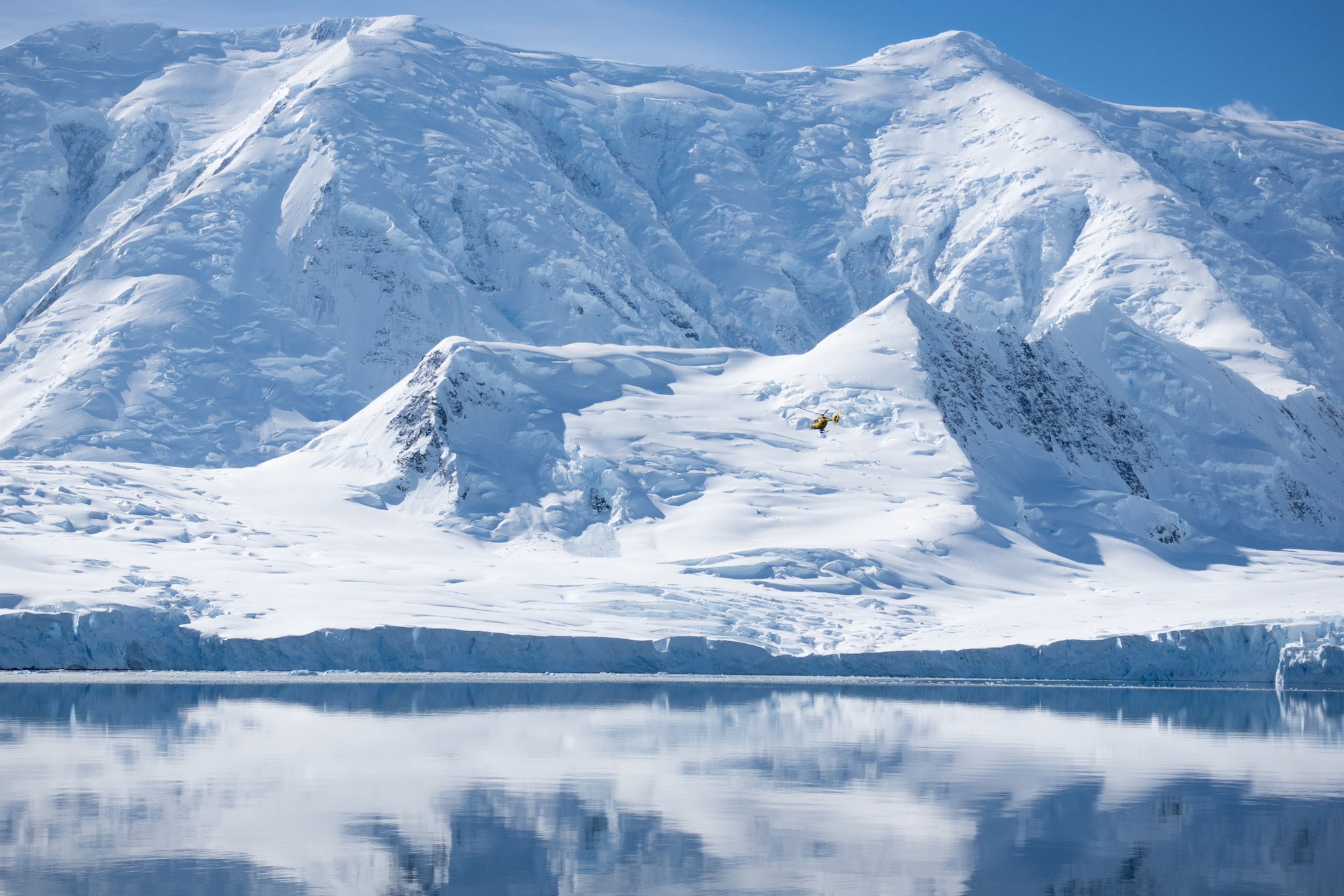 A small helicopter looks like a tiny speck against the huge Antarctic mountains