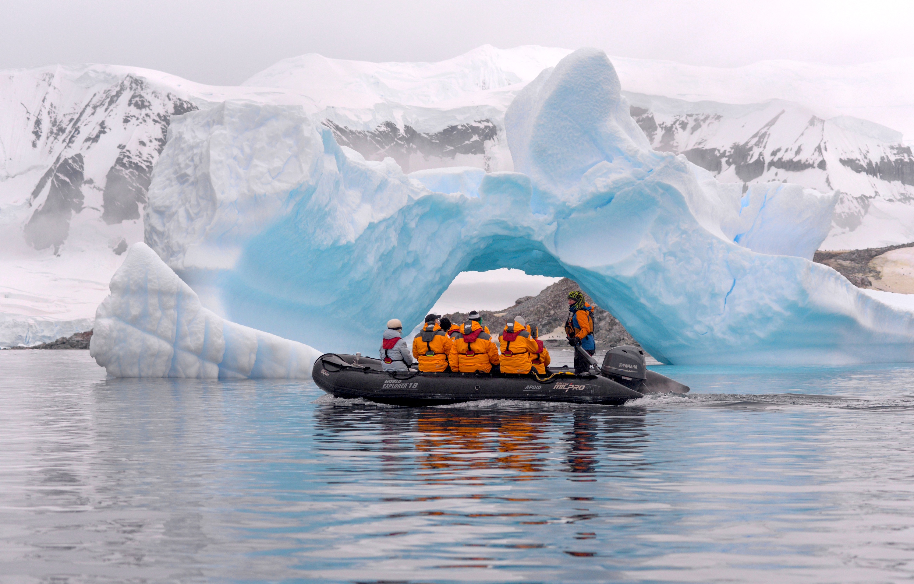 A zodiac cruises in front of an ice arch in Cuverville