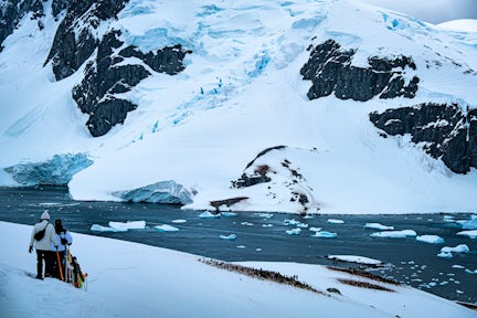 Snowshoers walk down a hill towards ice-covered water and mountains in Antarctica
