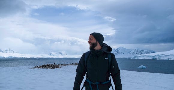 A man stands on the Antarctic Continent with penguins in the background