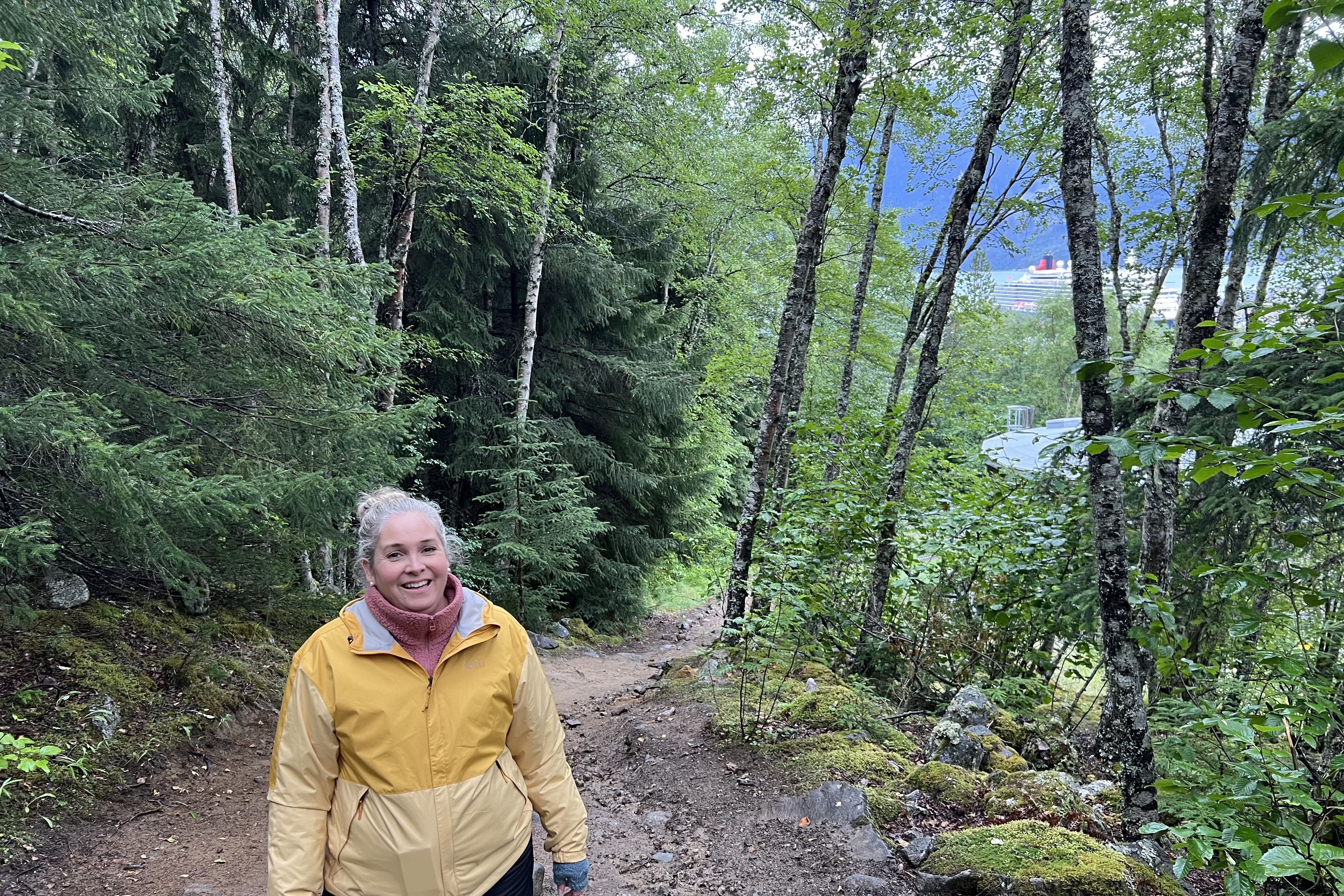 Angie standing at the top of a forest hill, looking down into trees with a ship in the distance